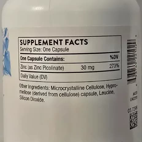 Thorne Zinc Picolinate capsules spilling from a white supplement bottle onto a warm wooden surface.
