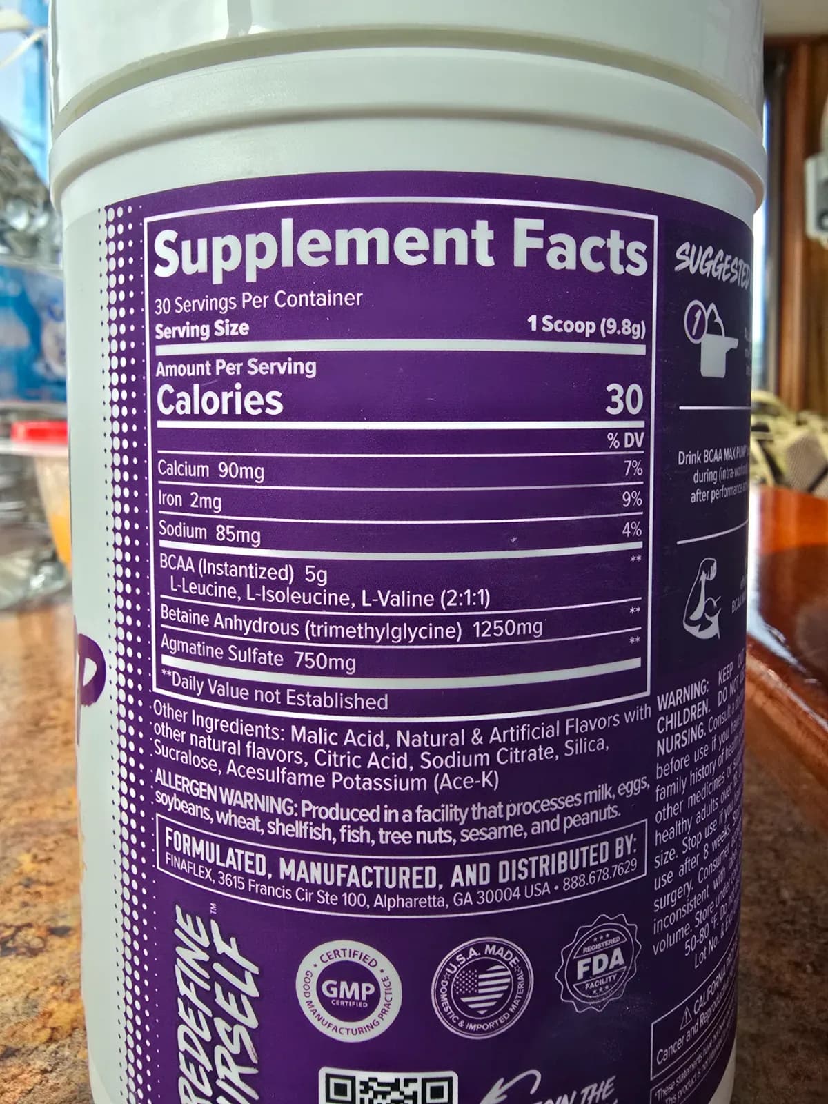 BCAA supplement tub and scoop next to a small stack of cash on a wood surface