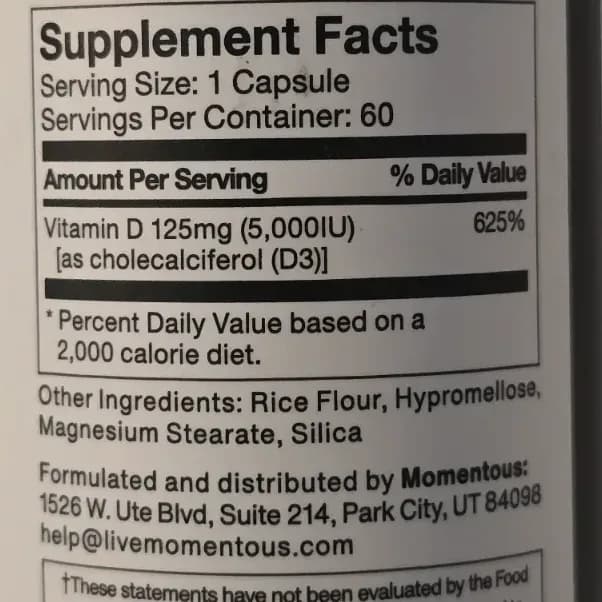 Small Momentous Vitamin D3 vegetable capsules next to the supplement bottle on a white surface.
