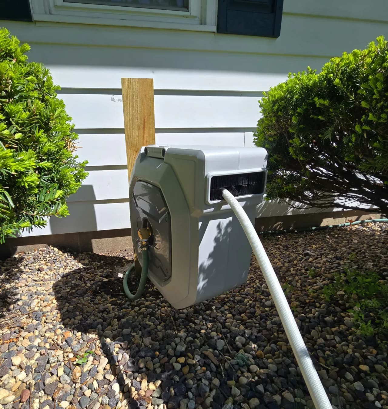 Hozereel retractable hose reel with included spray nozzle on a patio rail, garden background, morning light